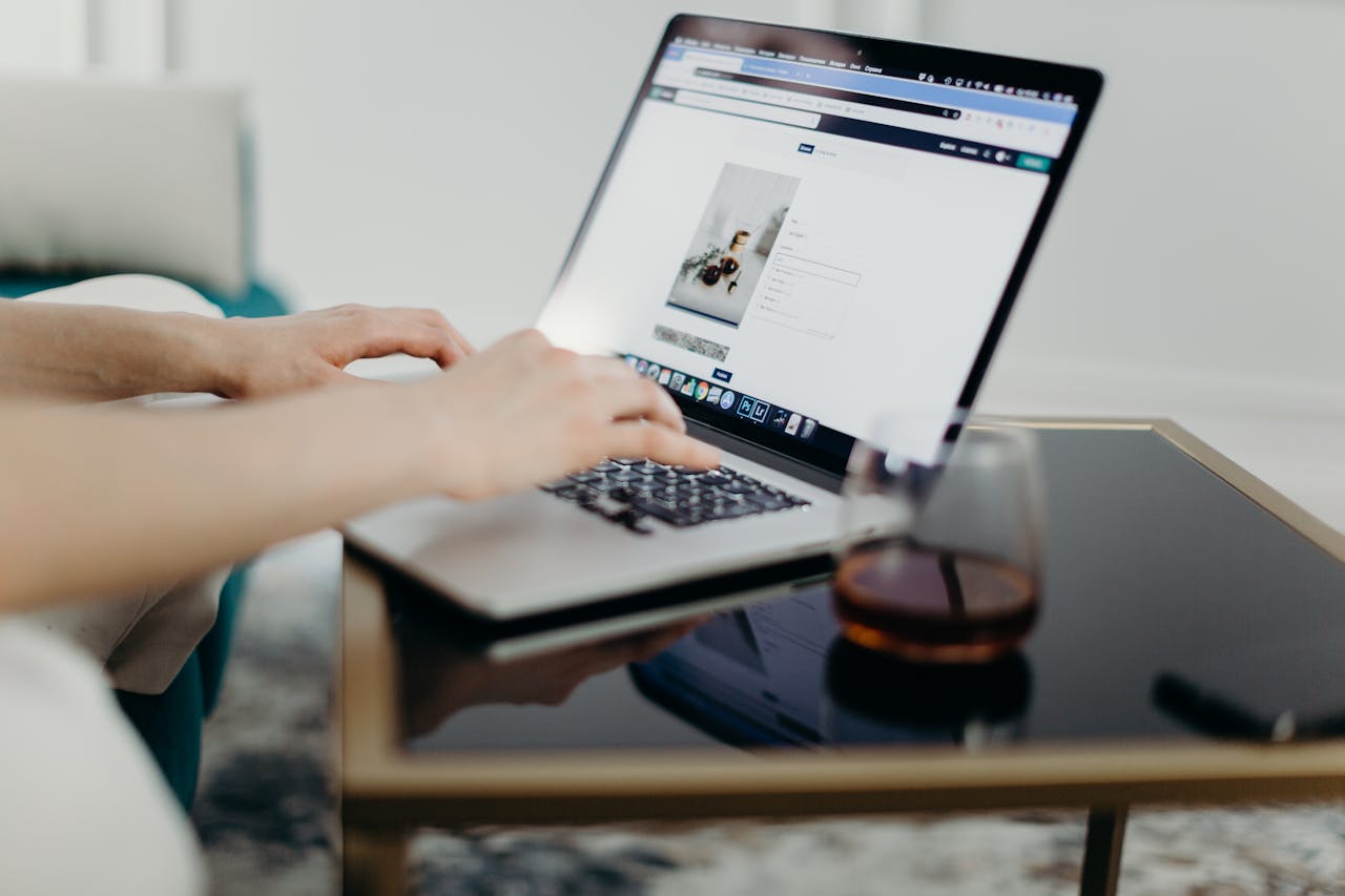 Home A person typing on a laptop in a stylish home office with a glass of drink nearby.